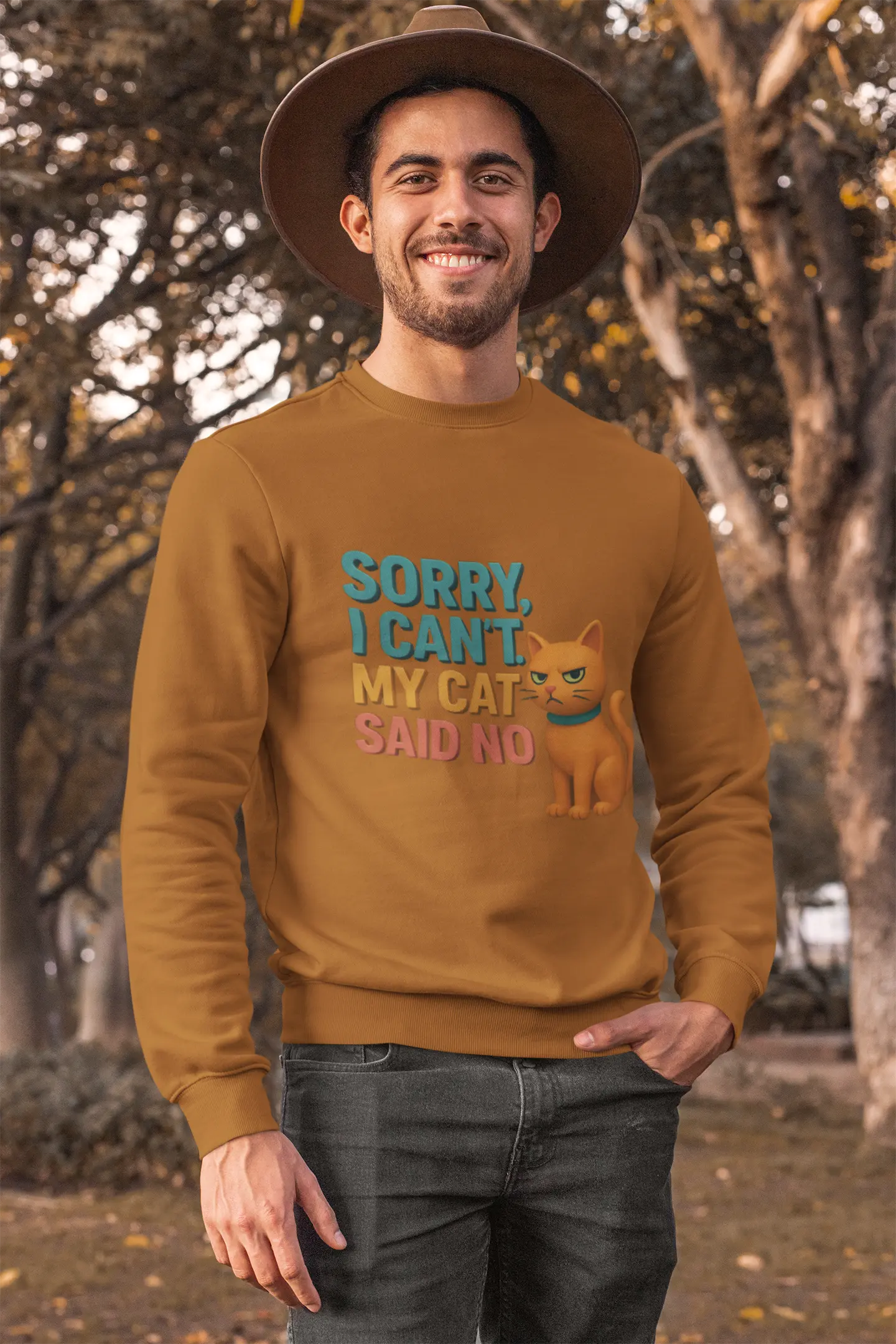 Sweatshirts men in a mustard yellow/ochre color featuring a funny graphic that reads "Sorry, I Can't. My Cat Said No." A man wearing a sweatshirt and a hat poses outdoors.