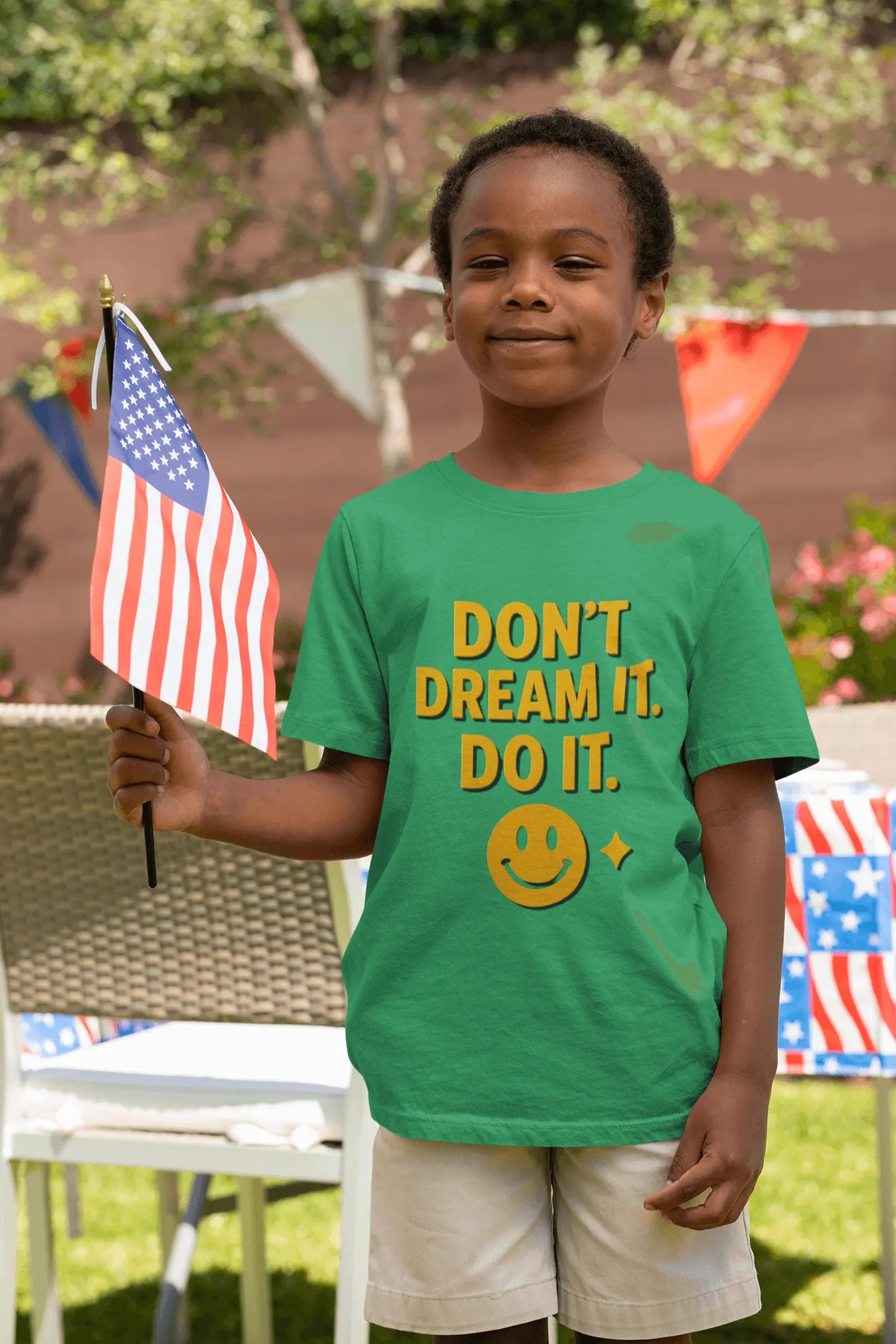 Bright green boys t shirts featuring a bold orange and yellow "Don't Dream It. Do It." motivational graphic. A young boy holds an American flag outdoors during a celebration.